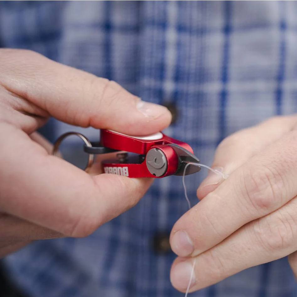 Person using a red plier with a thread against a blue checkered background