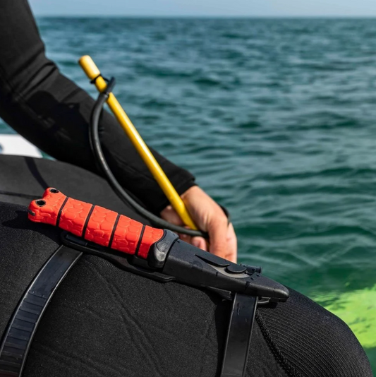 Person in wetsuit holding a red and black tool with ocean in background