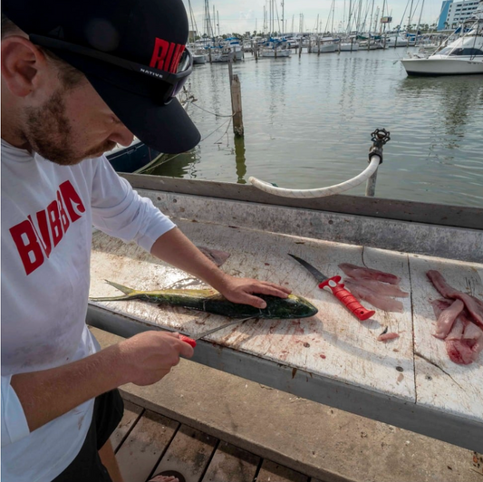 Man cleaning fish on a marina dock with boats in the background