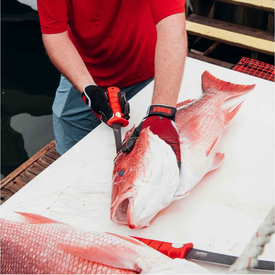 Person filleting a fish on a cutting board with a knife, wearing red gloves.