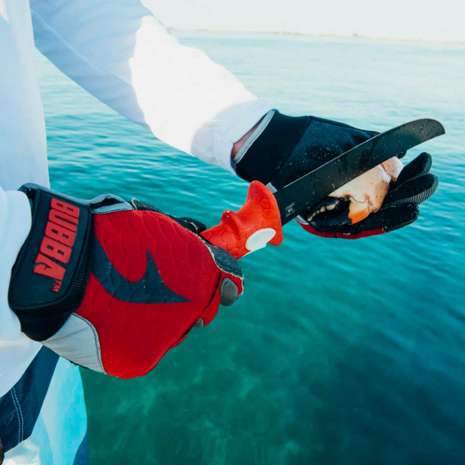 Person wearing red and black gloves with a visible brand logo, holding onto a rope against a water background.