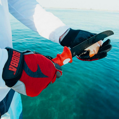 Person wearing red and black gloves with a visible brand logo, holding onto a rope against a water background.