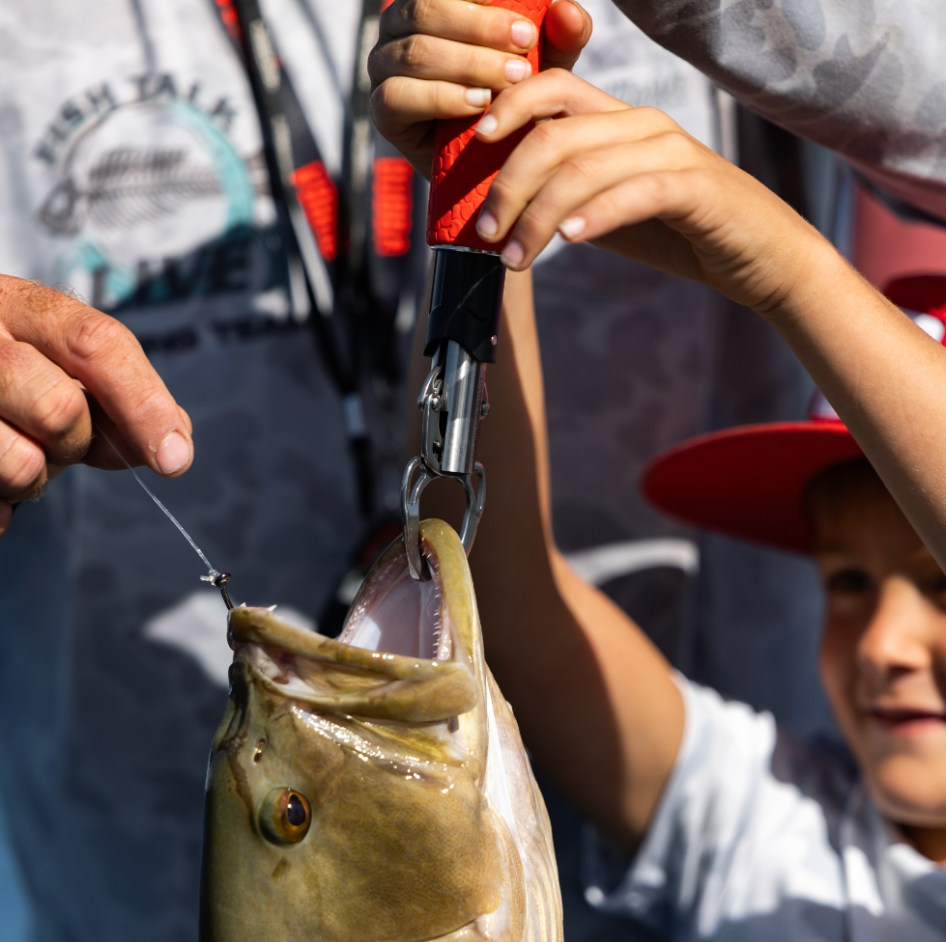 Person holding a fish caught on a hook with another person in the background