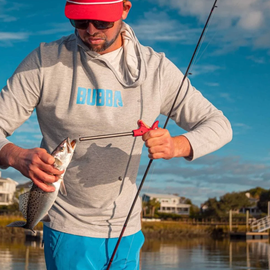 Man holding a fish and a fishing rod by a lake with 'Bubba' branding on his shirt.