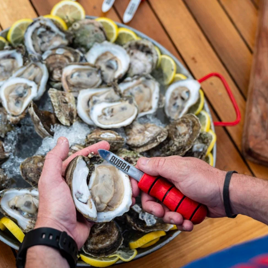 Person shucking oysters with a Bubba brand tool on a platter of oysters and lemons.