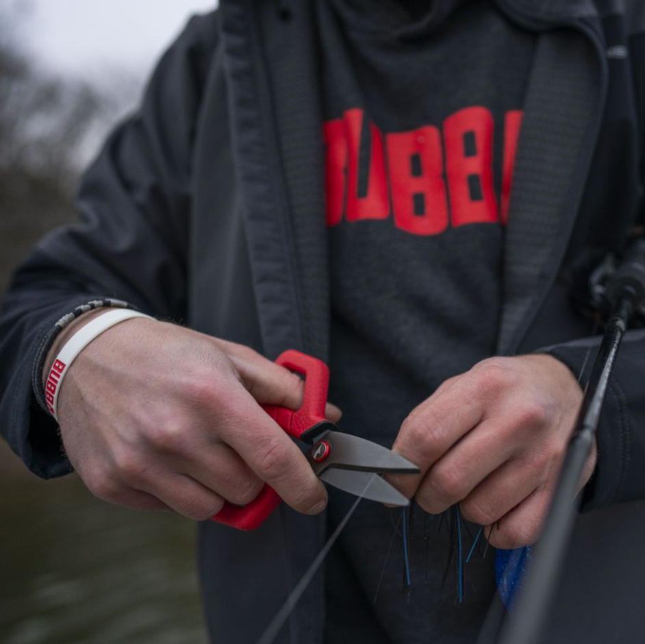 Person holding red-handled scissors with a blurred background