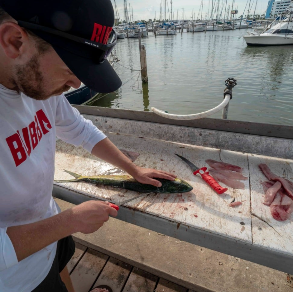 Man cleaning fish on a marina dock with boats in the background