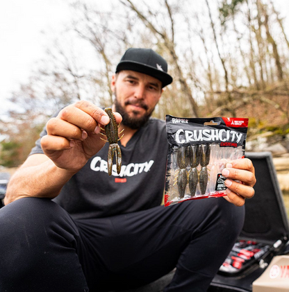 Man holding a fishing lure and packaging with 'Crush City' branding outdoors.