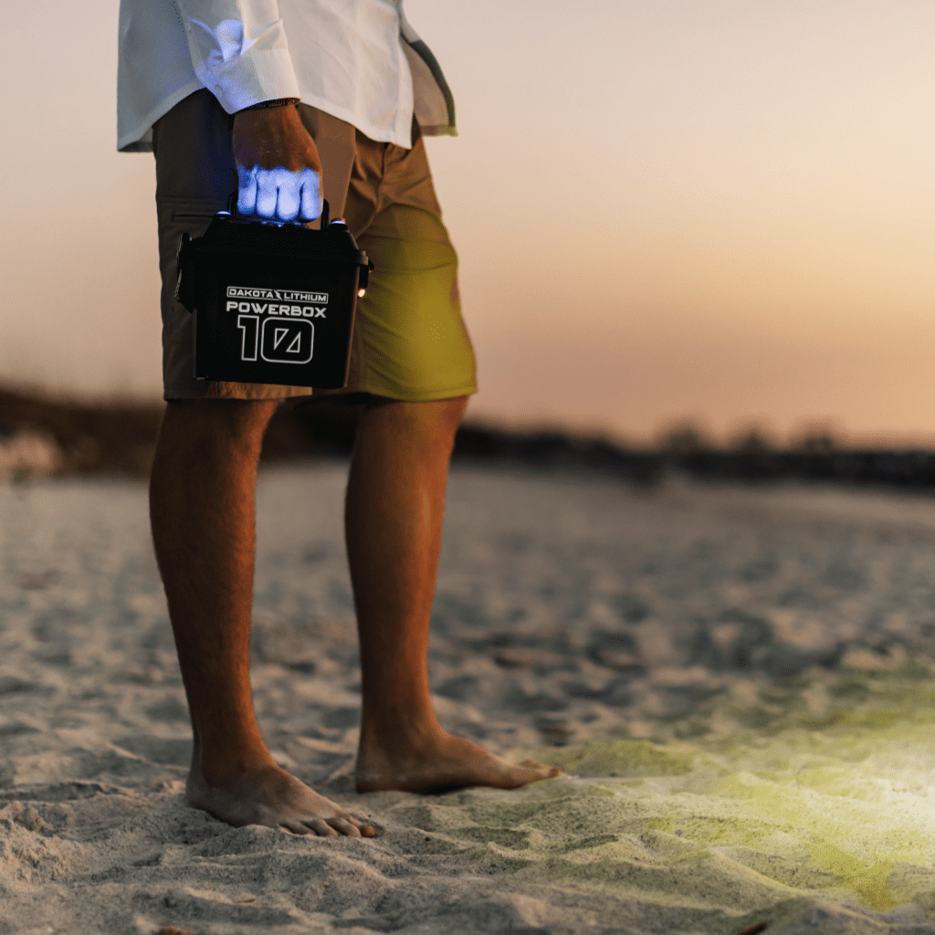 Person holding a PowerBox device on a beach at sunset