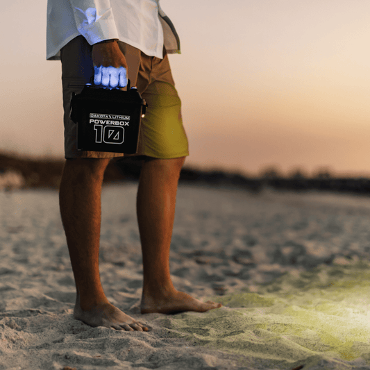 Person holding a PowerBox device on a beach at sunset