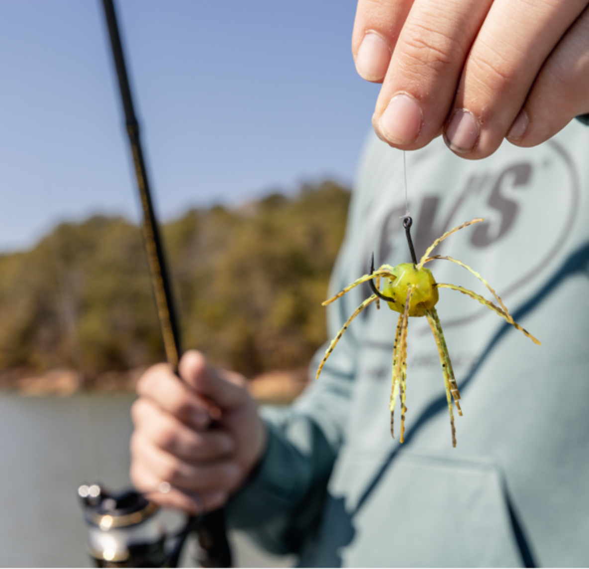 Person holding a fishing rod with a spider-shaped lure near a body of water.