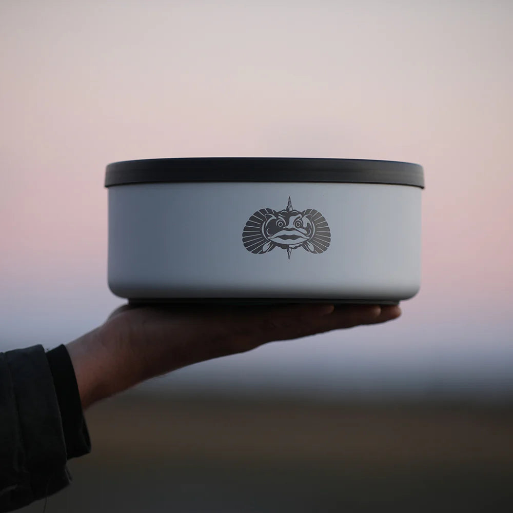 Hand holding a light blue bowl with a black lid against a blurred background