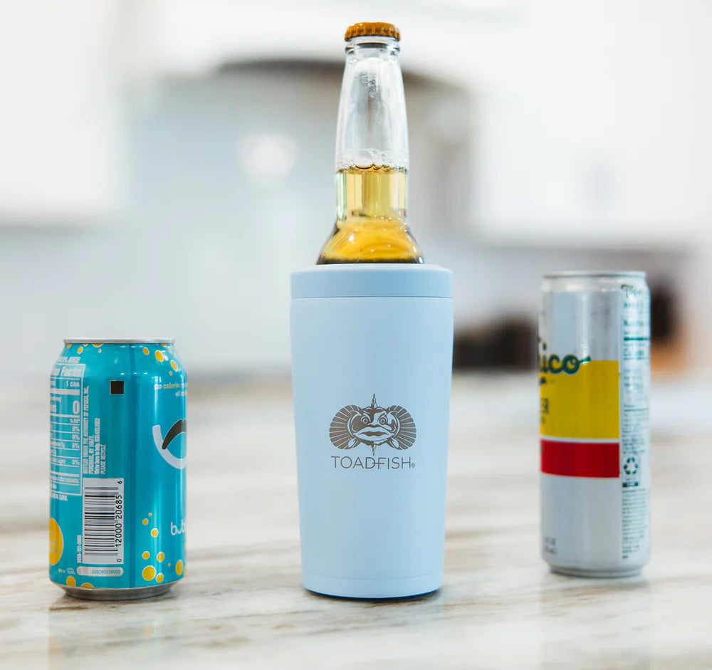 Glass bottle with a blue koozie, two cans on a light surface