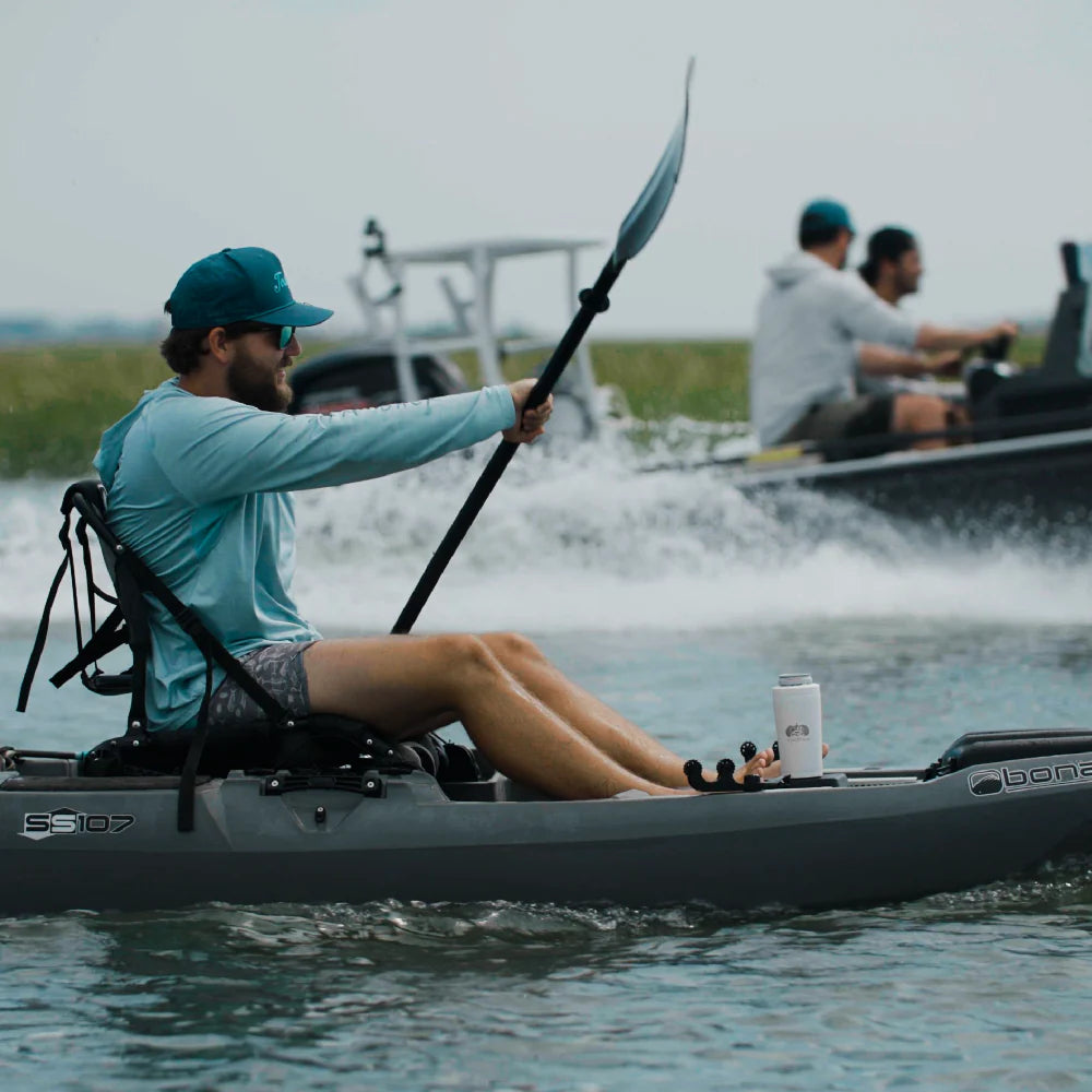 Person kayaking on a lake with another person in a boat in the background
