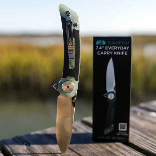 Folding knife with green handle and blade, next to its packaging box on a wooden surface with blurred natural background