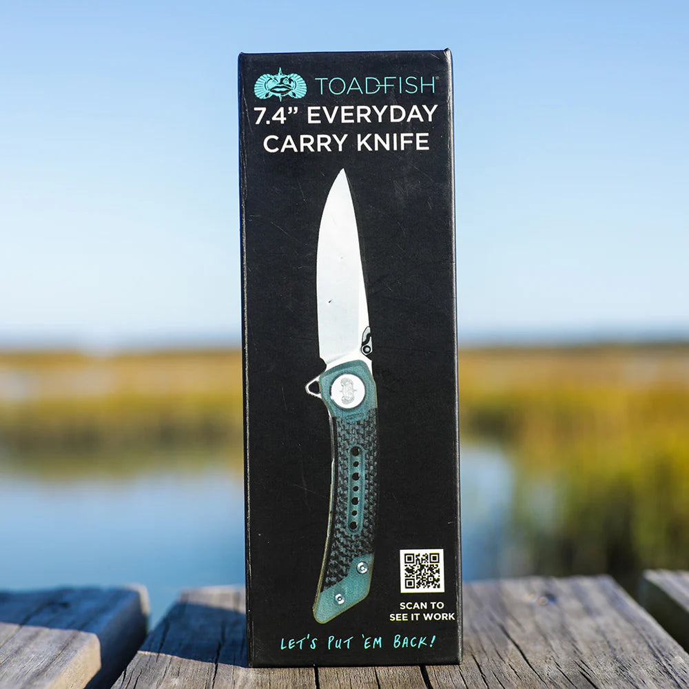 Box of a 7.4" Everyday Carry Knife by Toadfish on a wooden surface with a blurred natural background.