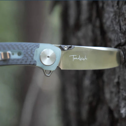 Folding knife with 'Toadfish' branding on a blurred natural background