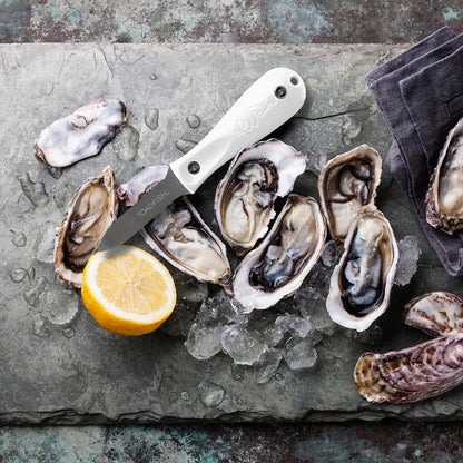 Open oysters on a bed of ice with a lemon wedge and knife on a dark surface.