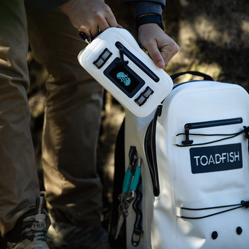 Person holding a white electronic device with a backpack labeled 'TOADFISH' in the background