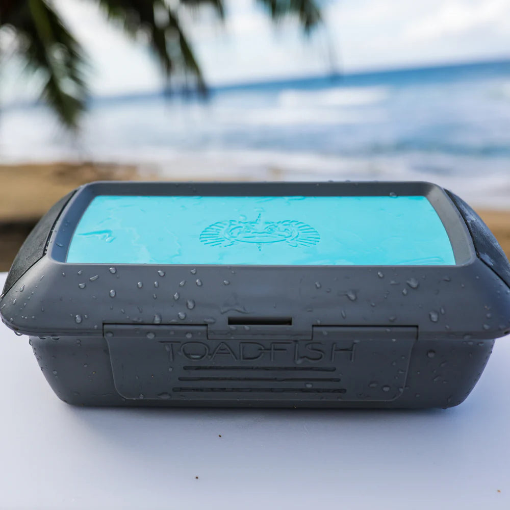 Black and blue tackle box with 'Toadfish' branding on a beach.