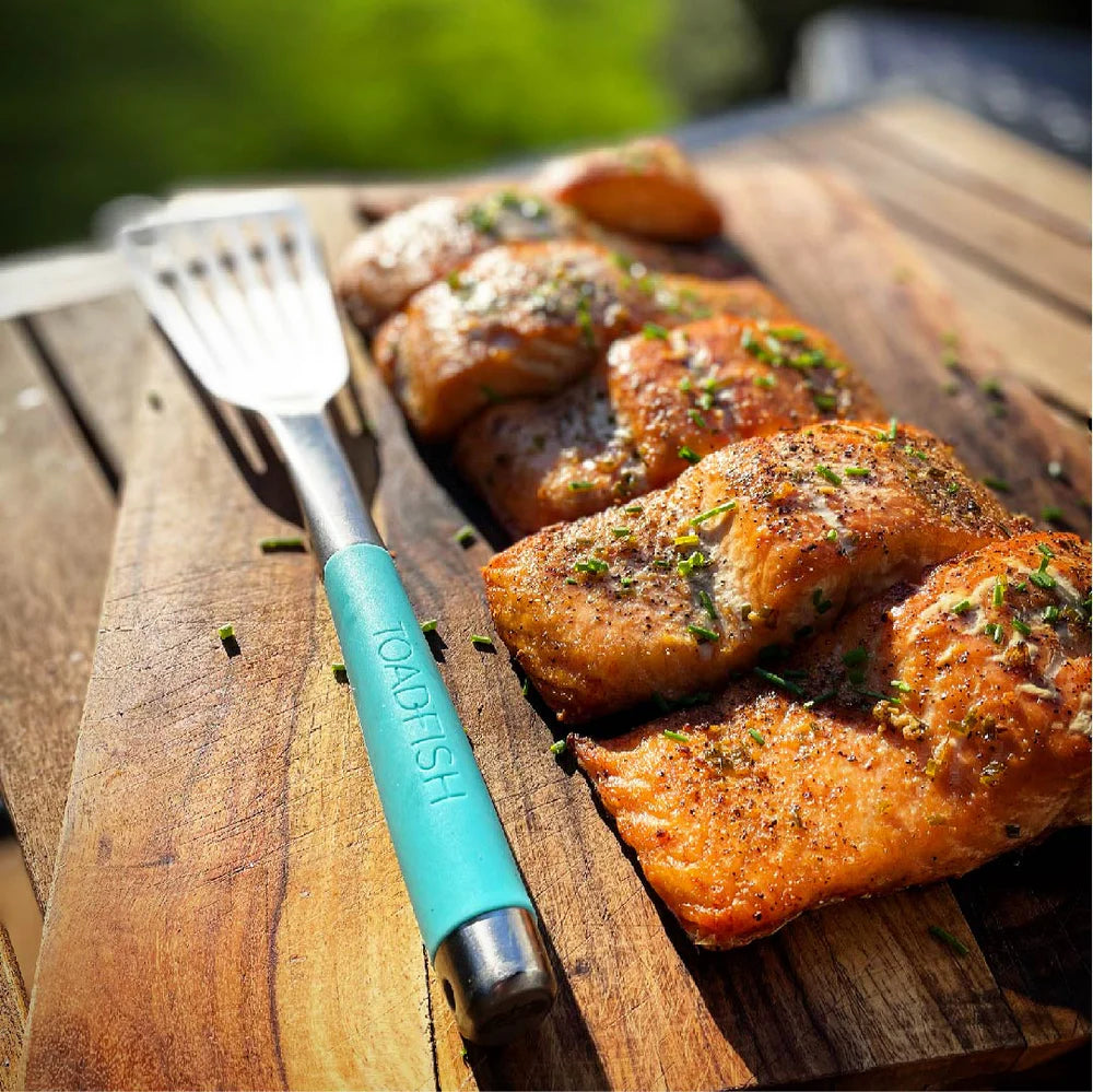 Grilled salmon fillets on a wooden cutting board with a spatula featuring 'TOASTFISH' branding.
