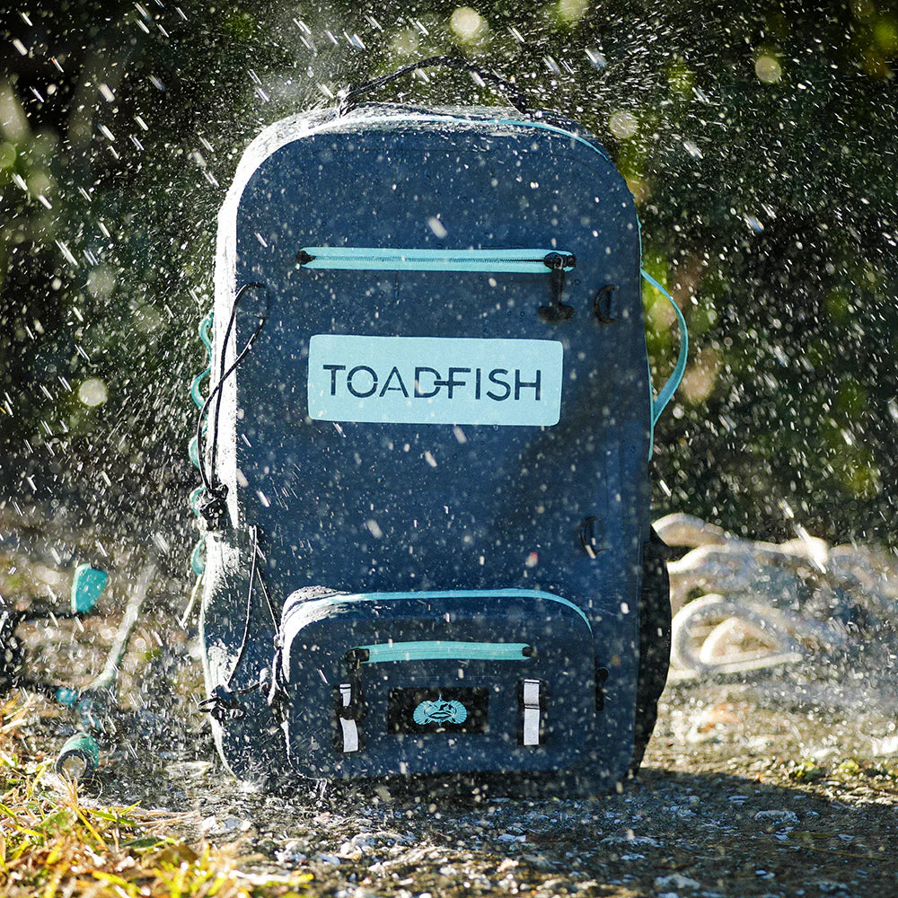 Blue backpack with 'TOADFISH' branding being splashed by water outdoors