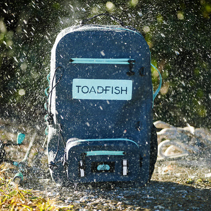 Blue backpack with 'TOADFISH' branding being splashed by water outdoors