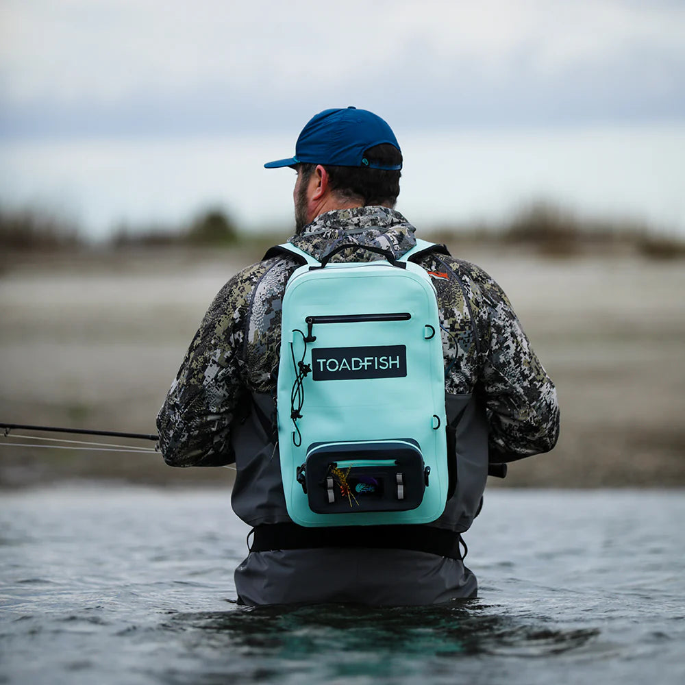 Man fishing in water wearing a teal backpack with 'Toadfish' branding.