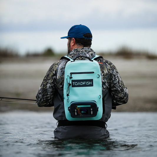 Man fishing in water wearing a teal backpack with 'Toadfish' branding.