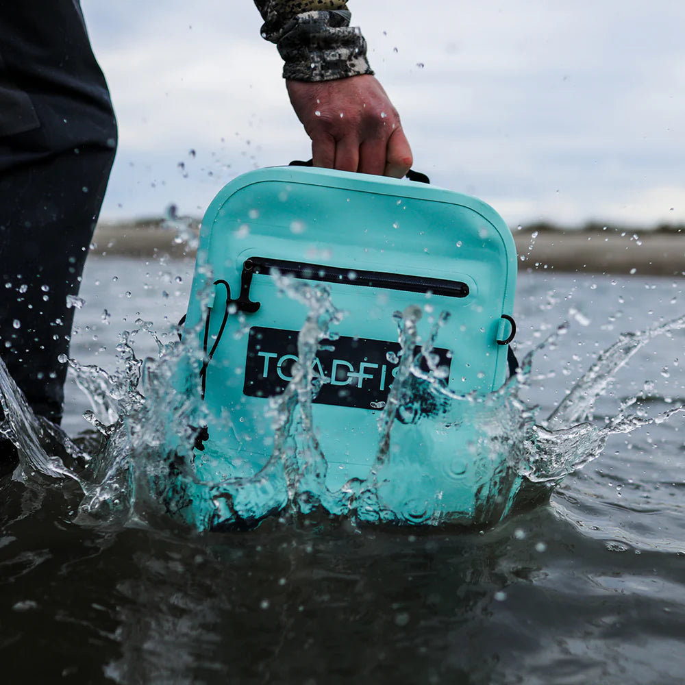 Turquoise cooler bag with 'TOADFISH' branding being submerged in water.