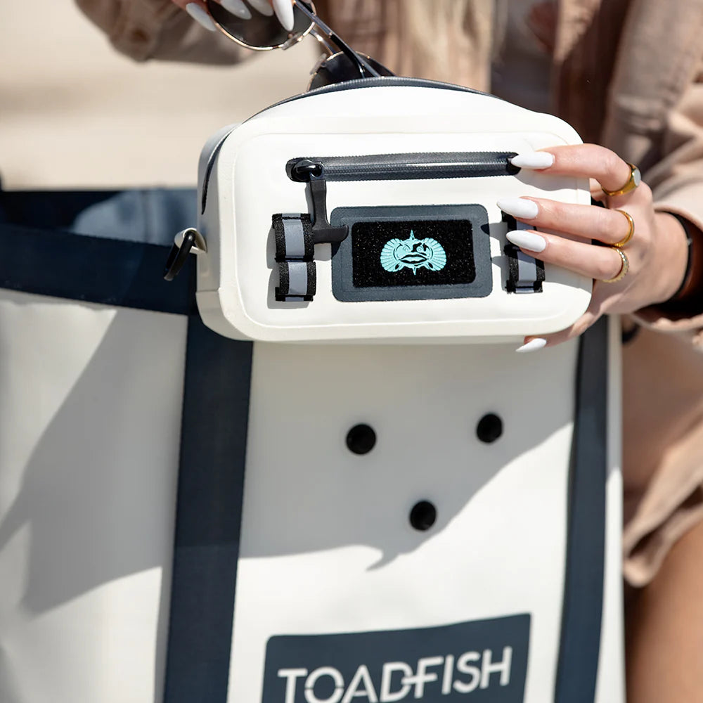 Person holding a white and black bag with 'Toadfish' branding.