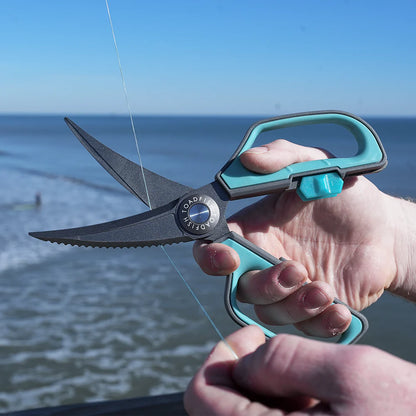 Person using large scissors with a blue handle by the ocean